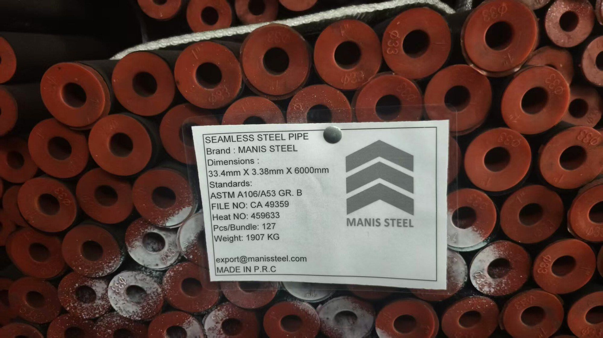 Seamless pipe bundle with red end caps and a Manis Steel tag: ASTM A106/A53 Grade B, 33.4 × 3.38 mm, 6 m lengths