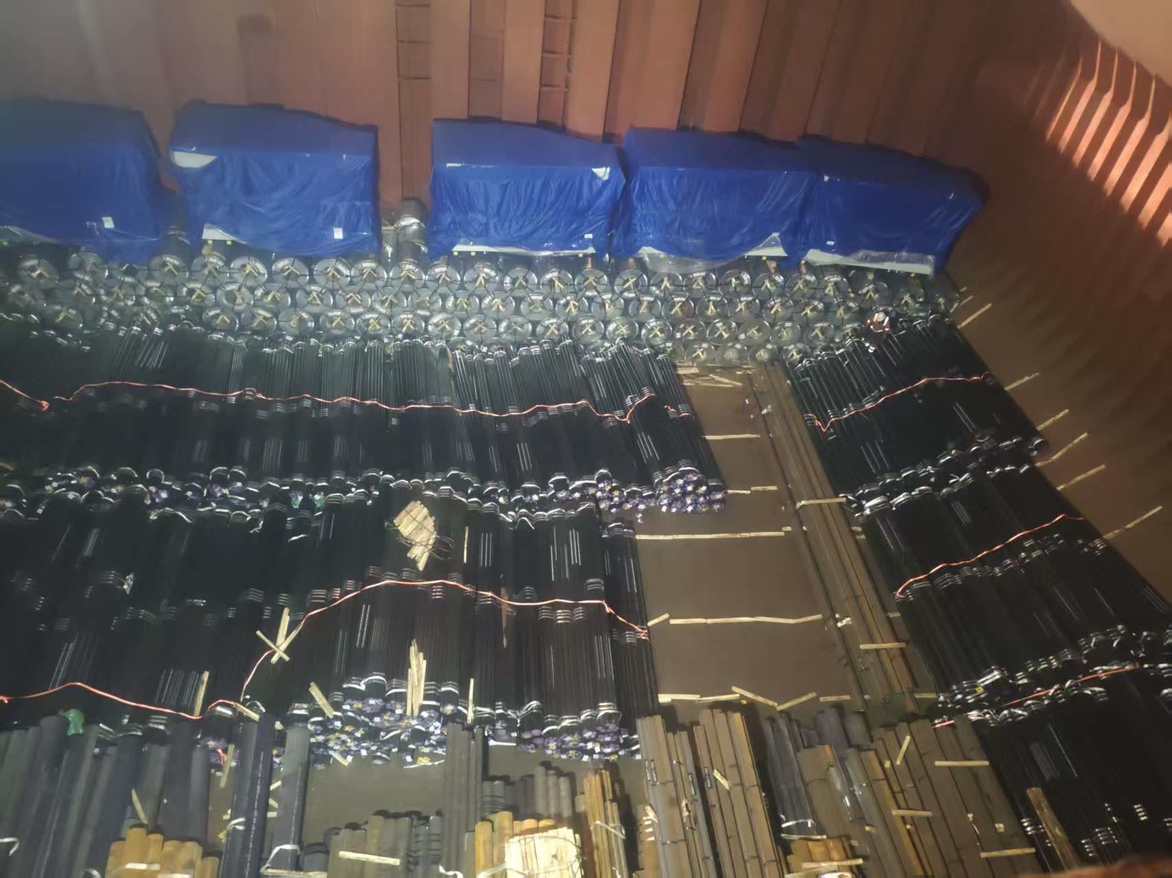 Pipe bundles stowed in a ship’s hold on timber dunnage, with tarpaulin-covered cargo above