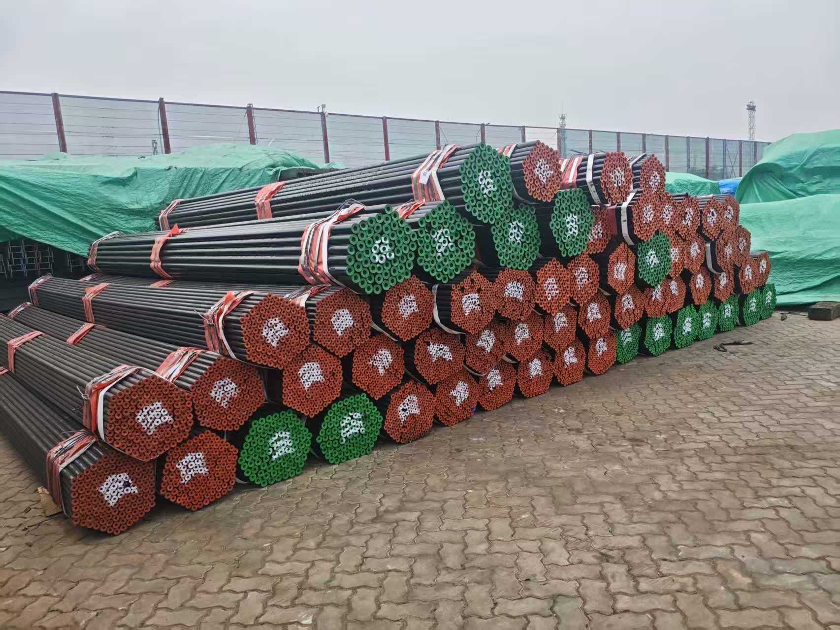 Long rows of seamless pipe bundles with red and green end caps in a fenced stockyard