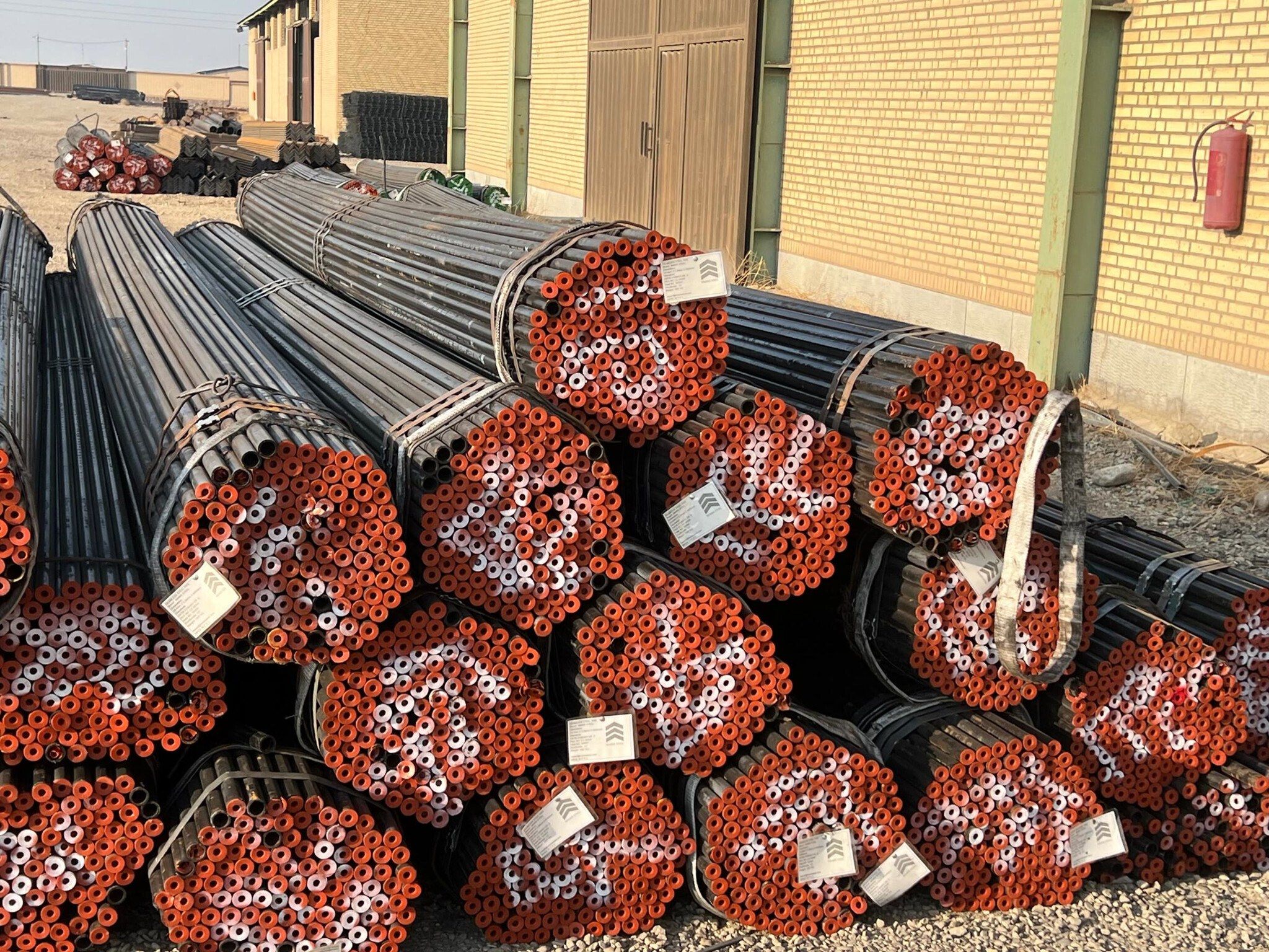 Bundles of seamless pipe with red end caps outside a warehouse in our sister brand’s Tehran yard